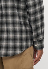 Zwart-wit geblokt flanellen shirt met lange mouwen, voorzien van een knoopsluiting bij de manchetten en een afgeronde zoom, gecombineerd met beige broeken.
