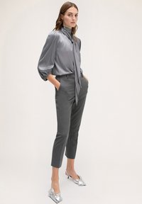 Blusa di raso grigia con maniche a sbuffo e colletto con nastrino, abbinata a pantaloni grigi a righe sottili e scarpe argento lucide.