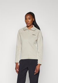 Lichtbeige fleecejack met rits en capuchon, voorzien van een klein logo op de borst en lange mouwen. Gladde textuur en aansluitend ontwerp.