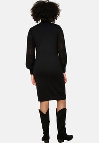 Abito nero con maniche lunghe in maglia a motivo, silhouette aderente, orlo fino al ginocchio, abbinato a stivali cowboy neri alti fino al ginocchio.