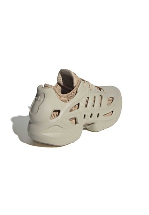 Beiger Sneaker mit einer skulptierten, belüfteten Außenschale und gepolsterter Innenfütterung, schräg dargestellt, um die Rück- und Seitenansicht zu zeigen.