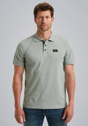Hellgrünes Poloshirt mit Kragen, einer Drei-Knopf-Leiste und einem kleinen schwarzen Logo-Patch auf der Brust. Kurzärmlig und mit geradem Saum.