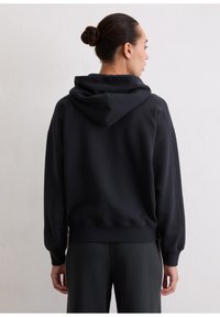 Zwarte hoodie met een ontspannen pasvorm, geribbelde manchetten en een geribbelde zoom. Kenmerkt zich door een getextureerd oppervlak en afgeplatte schouders. Achteraanzicht weergegeven.
