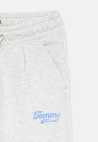 Lys grå joggebukser med teksturert stoff, med elastisk livbelte og sidelommer. Blå "Tommy"-logo på låret.