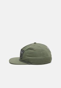 Cappello verde con visiera piatta, corpo in tessuto, etichetta nera sul davanti e un accento intrecciato testurizzato attorno alla base.