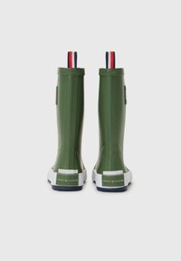 Bottes de pluie en caoutchouc vert avec semelles blanches, présentant une surface texturée, des talons rayés contrastants et un logo à l'arrière.