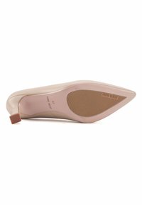 Zapato de tacón alto beige con punta afilada y suela de goma texturizada. Tacón resistente con una pequeña punta cuadrada, con el nombre de la marca grabado.
