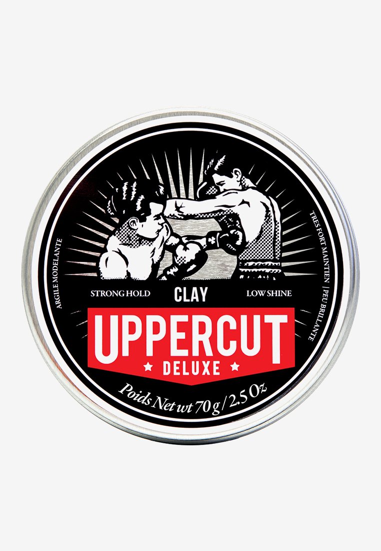 Rund metal dåse med sort og rød grafik, der viser to boksere. Etiket læser "Uppercut Deluxe," med teksten "Clay," "Strong Hold," og "Low Shine."