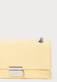 Sárga steppelt clutch, szintetikus anyagból készült; ezüst hardware-rel, fedele záródással és díszítő varrással rendelkezik.