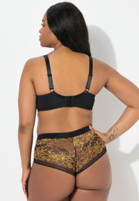 Schwarzer BH mit verstellbaren Trägern und Hakenverschluss, kombiniert mit schwarzen und goldenen Spitzenunterhosen mit floralem Muster und einem weichen Bund.