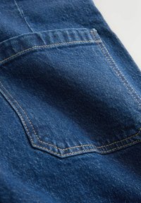 Džínovina tmavomodrej farby s výrazným zadným vreckom, viditeľným prešívaním a hladkou textúrou s miernymi odchýlkami.