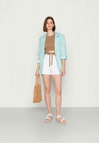 Blazer verde menta, top beige cropped, calções brancos de cintura alta, sandálias brancas e uma bolsa tecida em tom areia. Textura suave, design casual.