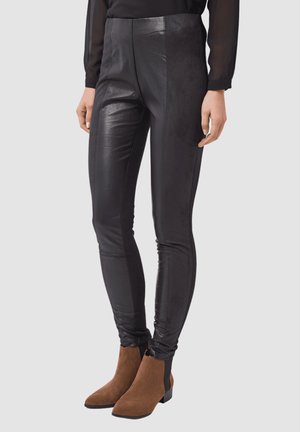 Leggings negros de piel sintética con cintura alta y ajuste ceñido, con un brillo sutil y paneles mate en contraste a lo largo de los laterales.