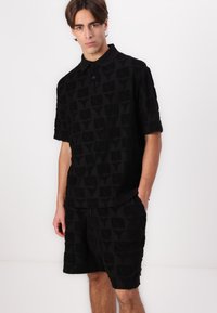 Black polo shirt and shorts set made of textured fabric with a subtle geometric pattern. Features a classic collar and short sleeves.