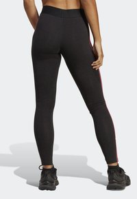 Svarta sportleggings med hög midja, med rosa sidostråk. Tyget ser slätt och elastiskt ut. Bärs med svarta sneakers.