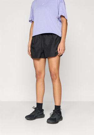 Μαύρες αθλητικές βερμούδες με υφή, συνδυασμένες με ένα ανοιχτό μωβ, ελαφρώς φαρδύ t-shirt και μαύρα αθλητικά παπούτσια.