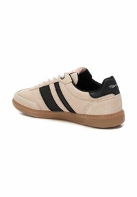 Sneaker in suede beige con righe in pelle nera. Presenta un sistema di allacciatura bianco, un interno imbottito nero e una suola in gomma marrone.