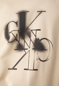 Tessuto beige con lettering astratto nero e accenti. Il design presenta lettere sovrapposte, creando un effetto visivo strati.
