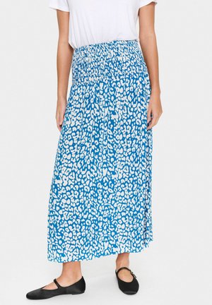Blauwe maxi rok met witte luipaardprint, gerimpelde tailleband, vloeiende stof en een brede silhouette. Gecombineerd met zwarte platte schoenen.
