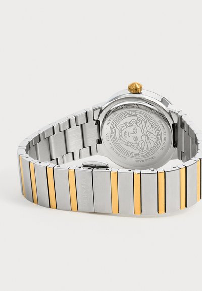 Montre bracelet en métal argenté et doré avec tête de Méduse gravée sur le fond en acier inoxydable et couronne dorée sur le côté.