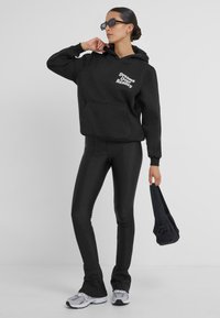 Zwarte hoodie met witte tekst "Dreams Over Reality", gecombineerd met strakke zwarte broek en grijze sportieve schoenen, met een zwarte tas.