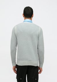 Ανοιχτό γκρι πλεκτ�ό πουλόβερ με ριγωτά μανίκια και κεντρί. Διαθέτει στρογγυλή λαιμόκοψη και μακριά μανίκια. Φοριέται πάνω από μια μπλε πουκάμισο.