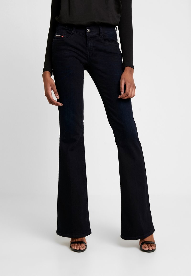 Mörkblå utsvängda jeans med medelhög midja, tillverkade av denimtyg. Har bältesöljor, framknäppning och två påsydda fickor.