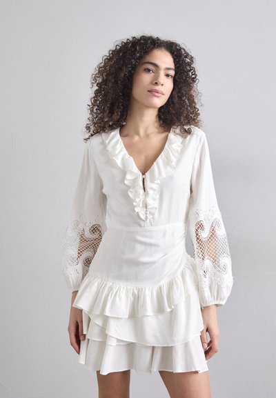 Robe blanche à volants avec de longues manches en dentelle, un décolleté en V et une jupe en tissu à plusieurs niveaux. Présente des détails en dentelle délicate et une texture douce.