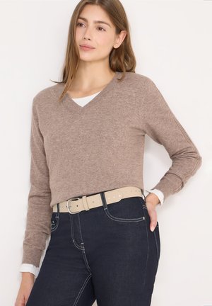 Beige trui met V-hals, gemaakt van zacht materiaal, gecombineerd met donkerblauwe spijkerbroek en een lichtbeige riem. De trui heeft lange mouwen en geribbelde manchetten.