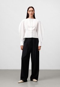 Witte cropped blouse met pofmouwen, gedragen met hoge taille zwarte broeken. De blouse heeft een voorpand met knopen en een minimalistisch design.