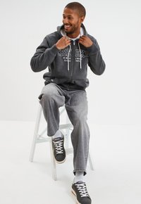 Sudadera gris con cremallera y letras blancas, combinada con jeans sueltos de un gris claro y zapatillas grises. Diseño simple, ajuste casual y textura suave.