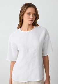 Top in lino bianco con scollo rotondo e maniche corte. Il tessuto ha una texture morbida e una sottile trama, offrendo una vestibilità comoda.