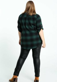 Zielono-czarna flanelowa koszula w kratę z podwiniętymi rękawami, zestawiona z dopasowanymi czarnymi skórzanymi spodniami oraz brązowymi botkami na obcasie.