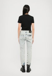 Svart t-skjorte med korte ermer kombinert med lyseblå jeans som har en baklomme og et svart logo-patch nær midjen. Sorte ankelstøvler.