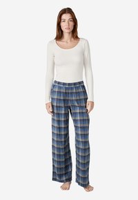Pantalones de pijama de cuadros largos en azul con líneas amarillas y negras, combinados con una camiseta de manga larga ajustada blanca de canalé. Material de algodón, corte relajado.