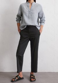 Ljusblå lin skjorta med mandarin krage, långa ärmar och svarta smala byxor. Svarta sandaler med en detalj av guldspänne.