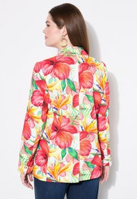 Farbiger Blumenblazer mit großen roten Hibiskusblüten und gelben Blättern auf weißem Hintergrund, mit taillierter Passform und Knopfdetails an den Ärmeln.