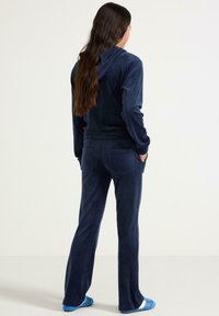 Marineblaues Velour-Trainingsanzug mit Kapuzenjacke und passender Hose. Der Stoff hat eine glatte Textur; die Hose verfügt über Gesäßtaschen.