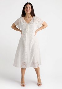 Weißes Kleid aus Lochstickerei mit einem V-Ausschnitt, kurzen Ärmeln und einer Länge bis zur Mitte der Waden. Dekoratives Muster im gesamten Kleid.