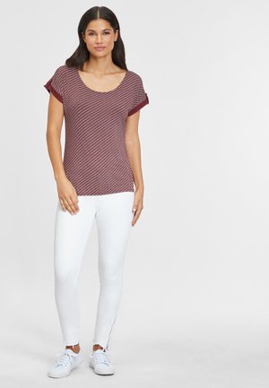 Red patterned short-sleeve top with a scooped neckline, paired with white skinny jeans and white sneakers. Simple and casual design.