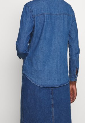 Denim overhemd in diep blauw met een gebogen zoom, knoopmanchetten en een klassieke kraag. Beschikt over een achterpand en zachte, getextureerde stof.