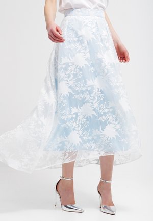 Jasnoniebieska midi spódnica w kwiaty z przezroczystą nakładką, wyposażona w szeroki pas i zwiewną sylwetkę. Połączona ze srebrnymi wysokimi obcasami.