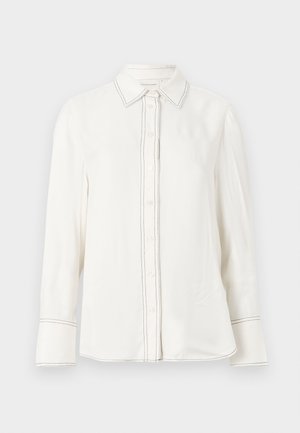 Hvit langermet skjorte i glatt stoff med knappelukking, spiss krage og kontrasterende svart søm langs plastrøret og mansjettene.