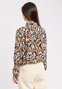 Long-sleeve shirt featuring a black base with a varied abstract pattern in cream and rust tones, finished with a collared neck and loose fit.