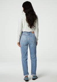 Lichtblauwe high-waisted jeans met een relaxte pasvorm, opgerolde manchetten en twee achterzakken. Gecombineerd met een witte top met blauwe stippen.
