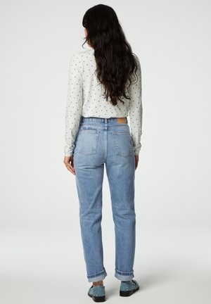 Lichtblauwe high-waisted jeans met een relaxte pasvorm, opgerolde manchetten en twee achterzakken. Gecombineerd met een witte top met blauwe stippen.