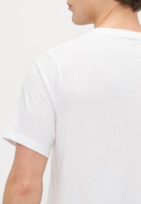 Balta medvilninė marškinėliai trumpomis rankovėmis ir apvali iškirpte. Audinys yra lygus ir kasdieniškas, be matomų raštų ar logotipų.