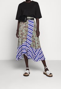 Černé tričko v kombinaci s midi sukní s různými vzory, která obsahuje paisley a modré pruhy. Doplněno bíle sandály na řemínky a černou ledvinkou.