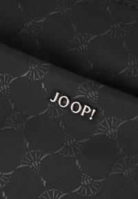 Svart textil med en subtil geometrisk mönster, med en metallisk silver "JOOP!" logotyp fäst. Slät struktur med mönstrad detalj.