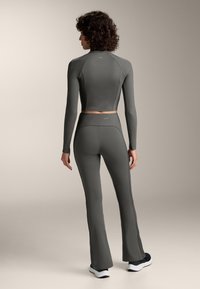 Tmavošedý priliehavý športový outfit s krátkym dlhým rukávom a vysokým pásom rozšírenými nohavicami, so štruktúrovanou tkaninou a kontrastnými švami.